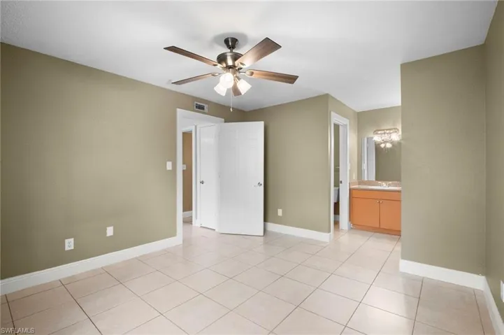 Unfurnished bedroom with ceiling fan, light tile patterned floors, and ensuite bathroom