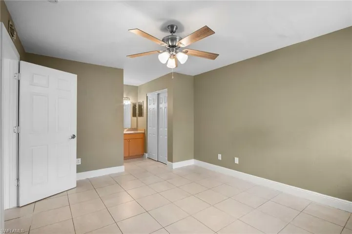 Unfurnished bedroom featuring ensuite bathroom, a ceiling fan, a closet, and light tile patterned floors