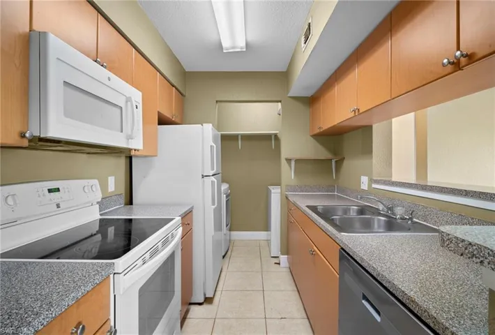Kitchen with white appliances, light tile patterned flooring, washer and clothes dryer, a textured ceiling, and brown cabinets