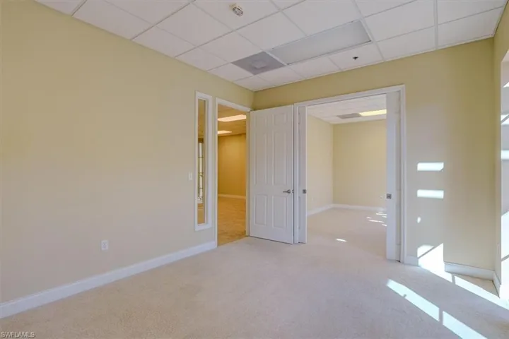Carpeted office with a drop ceiling and baseboards