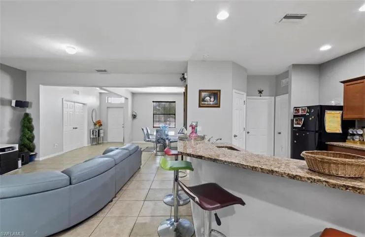 Kitchen featuring stone counters, black fridge, light tile floors, sink, and a breakfast bar area
