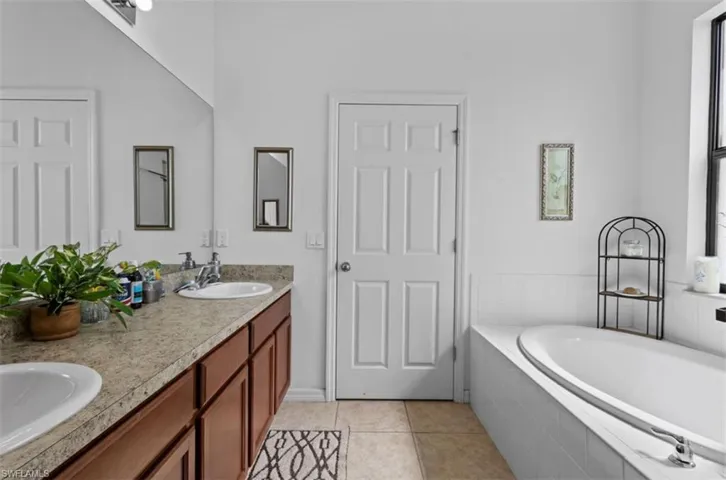 Bathroom featuring dual vanity, tiled bath, and tile flooring