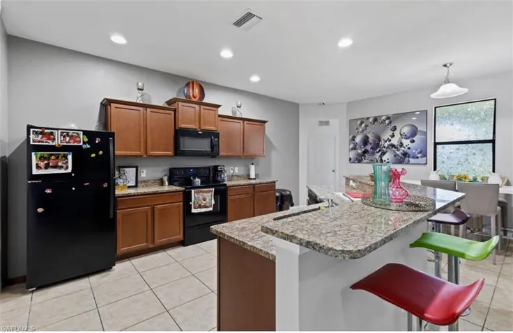 Kitchen featuring a kitchen breakfast bar, black appliances, light tile floors, hanging light fixtures, and sink