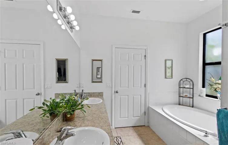 Bathroom with tiled bath, oversized vanity, dual sinks, and tile floors