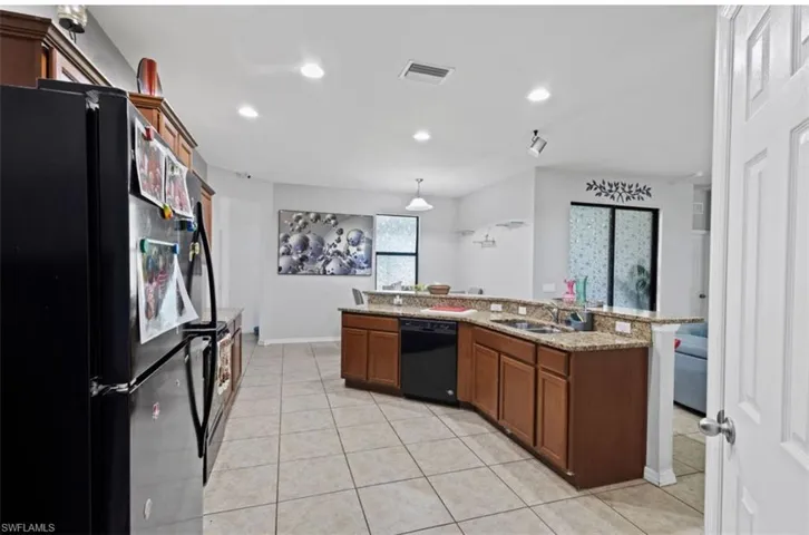 Kitchen with black appliances, light stone counters, pendant lighting, sink, and light tile flooring