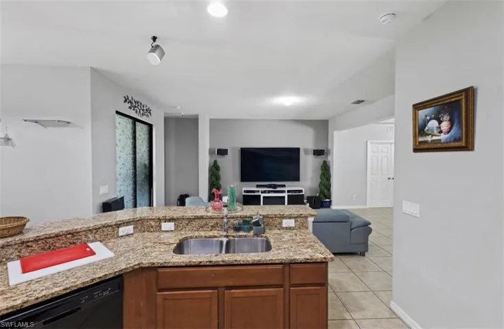 Kitchen with light stone countertops, sink, black dishwasher, and light tile flooring