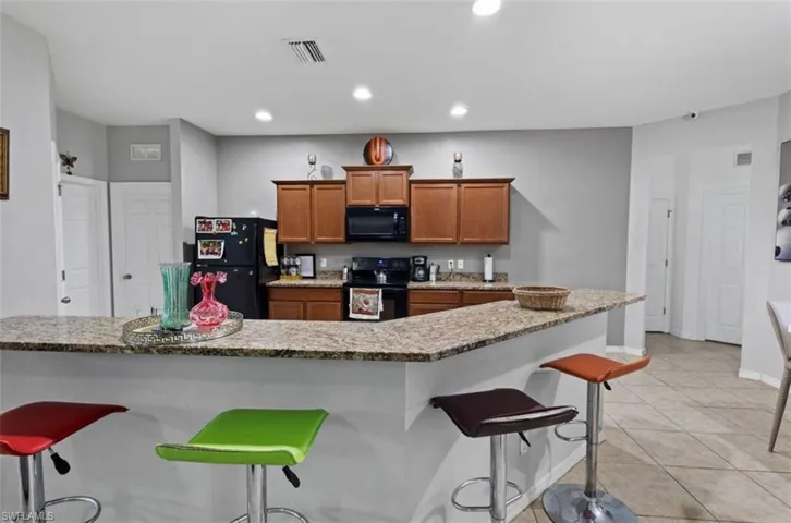 Kitchen with a kitchen island, light stone countertops, black appliances, light tile floors, and a breakfast bar