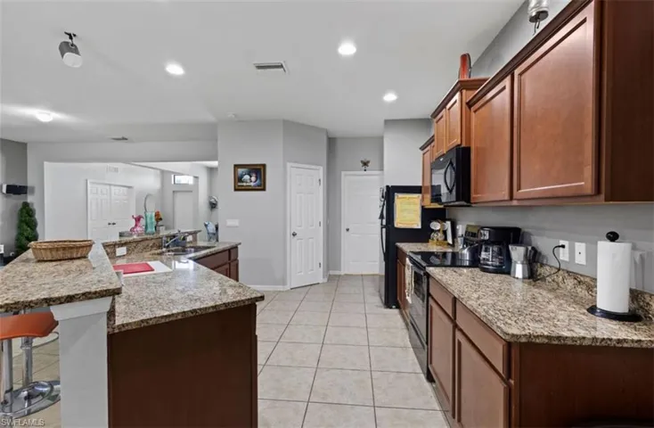 Kitchen featuring a center island with sink, stainless steel range with electric stovetop, light stone countertops, sink, and light tile floors