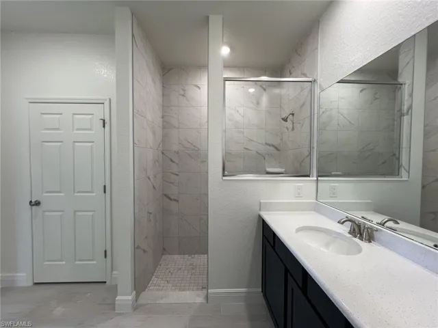 Full bath featuring vanity, a marble finish shower, and a textured wall