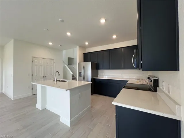 Kitchen featuring dark cabinetry, an island with sink, light stone counters, light wood-style floors, and recessed lighting
