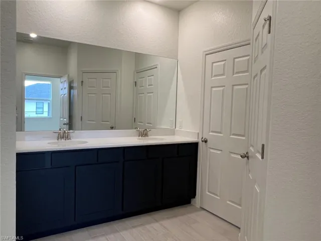 Bathroom with a textured wall, double vanity, and light wood-style floors