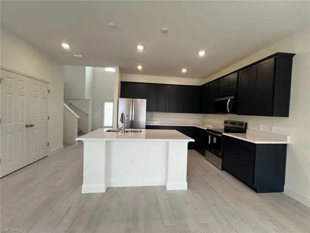 Kitchen with dark cabinetry, appliances with stainless steel finishes, light wood-type flooring, an island with sink, and recessed lighting