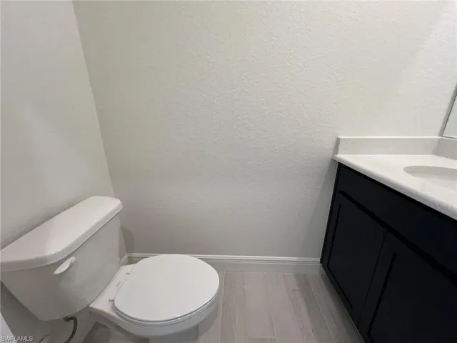 Half bathroom with vanity, a textured wall, and light wood-style floors