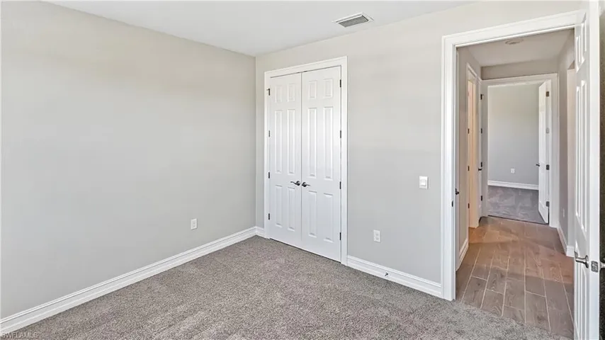 Unfurnished bedroom featuring a closet, wood finished floors, baseboards, visible vents, and carpet