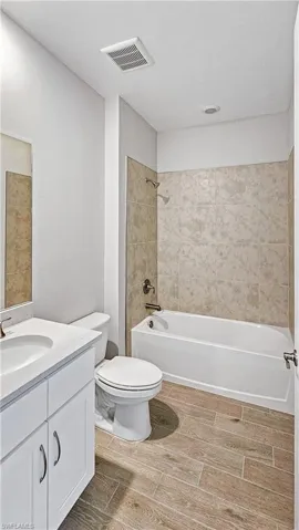 Full bathroom with toilet, vanity,  shower combination, wood tiled floor, and visible vents