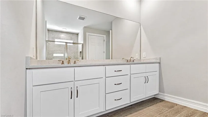 Full bathroom featuring visible vents, a shower stall, baseboards, double vanity, and wood tiled floor