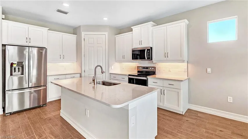 Kitchen with stainless steel appliances, a center island with sink, a sink, visible vents, and light wood-style flooring