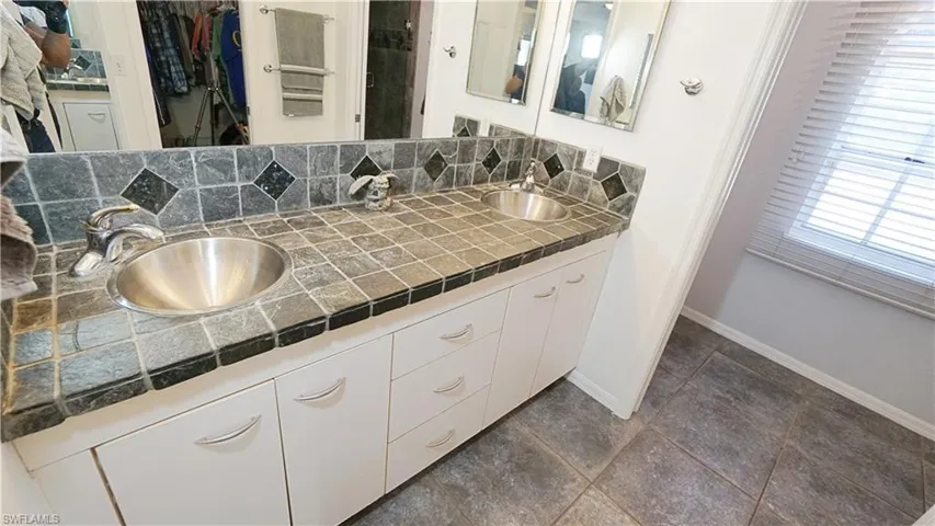 Bathroom featuring double vanity, baseboards, a walk in closet, and decorative backsplash