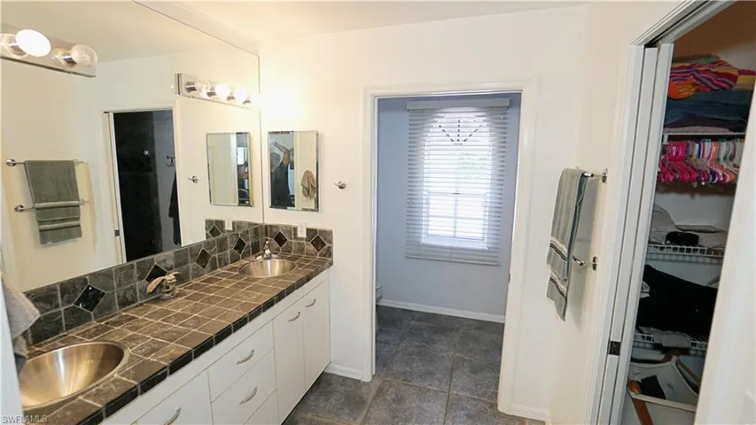 Bathroom featuring double vanity, a walk in closet, baseboards, and toilet
