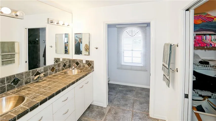 Bathroom with double vanity, a walk in closet, baseboards, toilet, and a shower