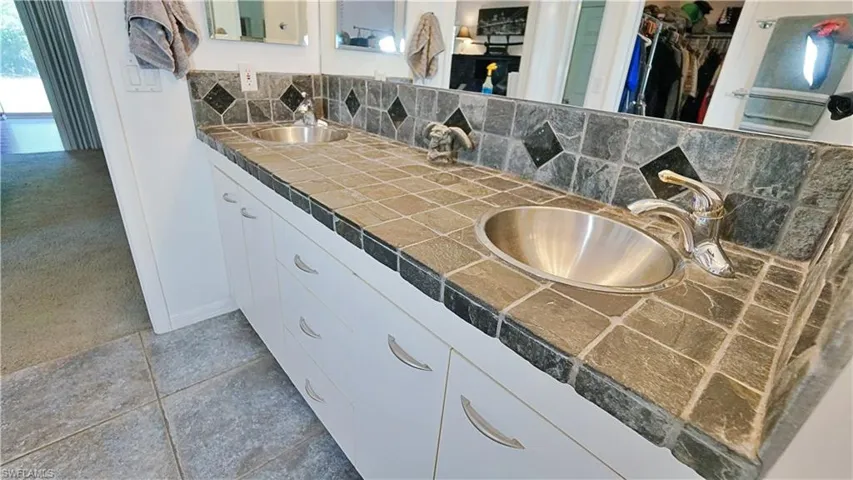 Full bath with decorative backsplash, double vanity, a spacious closet, tile patterned floors, and baseboards