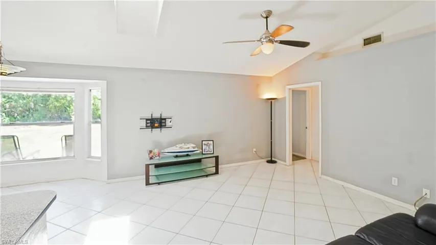 Living room with lofted ceiling, ceiling fan, light tile patterned floors, and baseboards