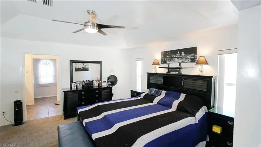 Carpeted bedroom featuring tile patterned floors, ceiling fan, and a raised ceiling