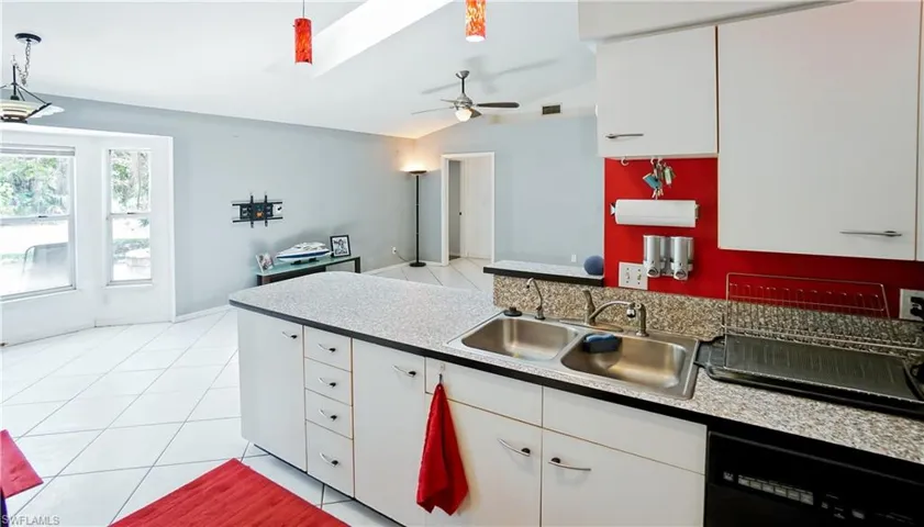 Kitchen featuring a sink, dishwashing machine, ceiling fan, lofted ceiling, and white cabinetry