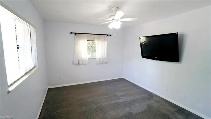 Empty room with a ceiling fan, baseboards, and dark carpet