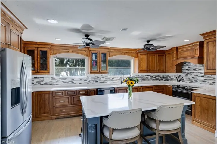 Kitchen with appliances with stainless steel finishes, a kitchen breakfast bar, brown cabinetry, light stone countertops, and recessed lighting