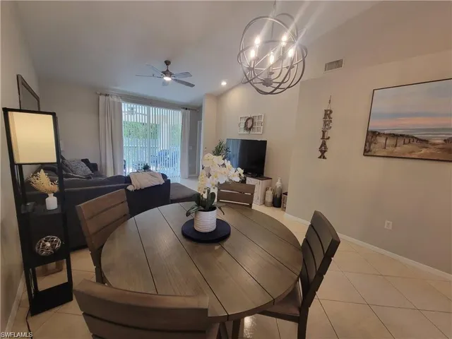 Dining area with a ceiling fan, a chandelier, light tile patterned floors, and vaulted ceiling