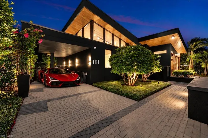 Modern architectural exterior featuring a gabled roofline with wood-plank soffits, expansive clerestory windows, a covered carport, and paved stone driveway