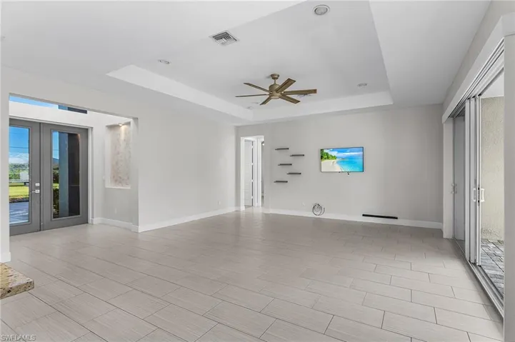 Empty room featuring a tray ceiling, french doors, ceiling fan, and wood tiled floors