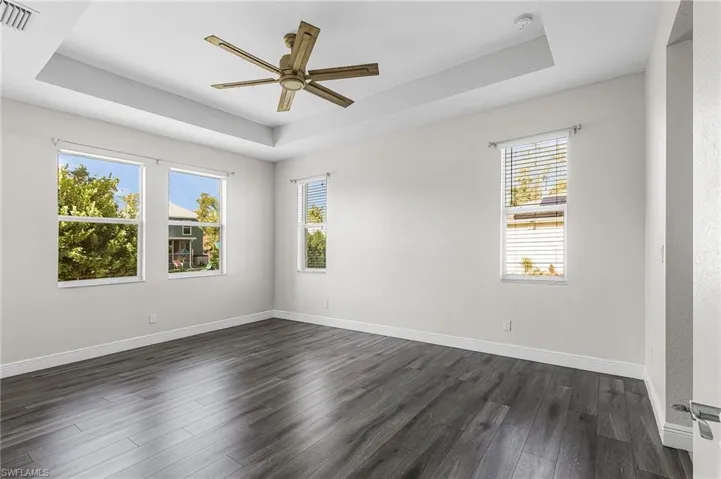 Master bedroom featuring a tray ceiling, dark wood-style flooring, and a ceiling fan