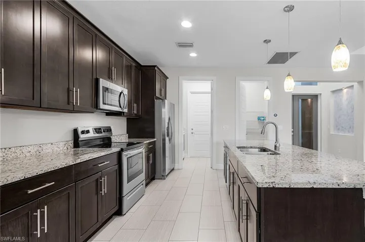 Kitchen with dark brown cabinetry, appliances with stainless steel finishes, light stone countertops, pendant lighting, and recessed lighting
