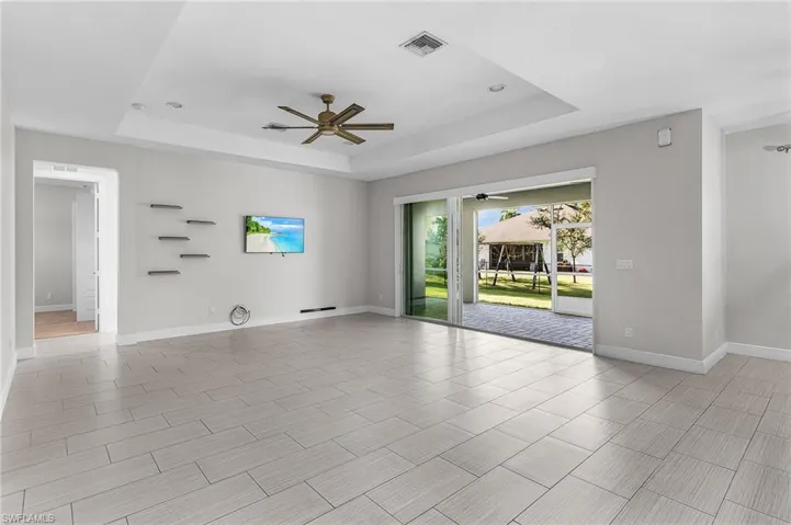 Empty room with a tray ceiling, ceiling fan, and wood finish floors