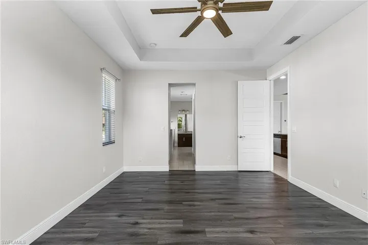 Master bedroom featuring a tray ceiling, dark wood-style floors, a ceiling fan, and ensuite bath