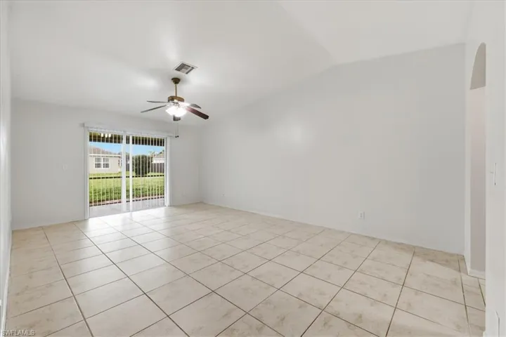 Spacious interior room featuring tile flooring, vaulted ceilings, a ceiling fan with integrated lighting, and a sliding glass door providing exterior access