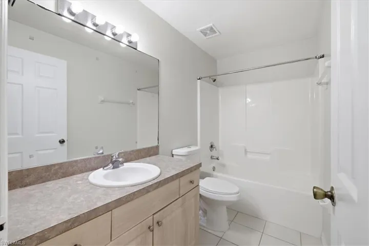 Bathroom featuring a wood-finish vanity with a laminate countertop, an integrated sink, and a large mirror with strip lighting