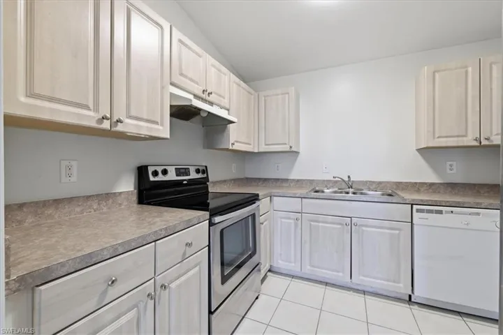 Kitchen featuring light wood-finish cabinetry, a stainless steel range with overhead ventilation, a double basin sink, and a white dishwasher