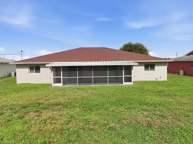 Rear exterior featuring a screened patio, a red shingle roof, light-colored stucco siding, and a spacious green lawn
