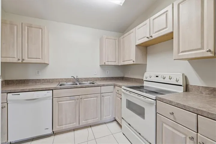 Kitchen featuring light-toned cabinetry, a double basin stainless steel sink, a white electric range, a built-in dishwasher, and a durable countertop