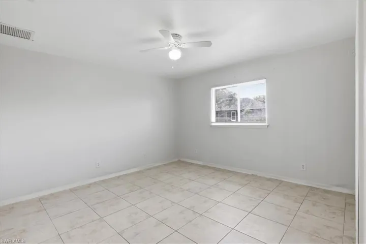 Spacious room featuring neutral tile flooring, a large window, a ceiling fan with integrated lighting, and light-toned walls