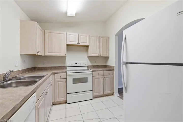 Kitchen featuring light wood-finish cabinetry, a double basin stainless steel sink, white electric range, white dishwasher, and a white refrigerator