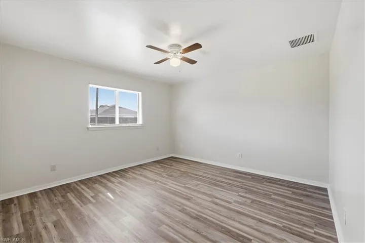 Spacious room featuring wood-finish flooring, a ceiling fan with integrated lighting, a double-pane window, and neutral wall paint