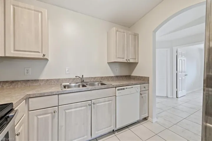 Kitchen featuring light-toned cabinetry, a double basin stainless steel sink with a chrome faucet, and a built-in white dishwasher