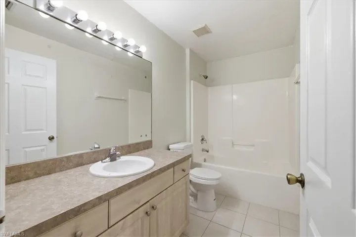 Full bathroom featuring a single vanity with an integrated sink, a large wall-mounted mirror, a tub/shower combination, and ceramic tile flooring