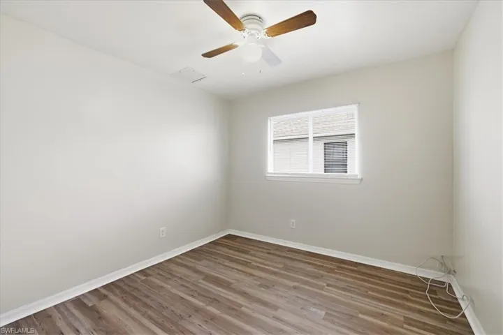 Spacious room featuring wood-finish flooring, light-toned walls, and a ceiling fan with wood-tone blades