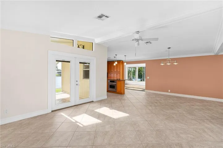 Unfurnished living room with light tile patterned floors, ceiling fan with notable chandelier, french doors, and beamed ceiling