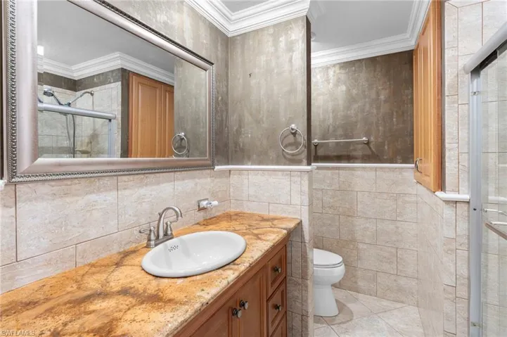 Bathroom with vanity, crown molding, an enclosed shower, tile walls, and toilet